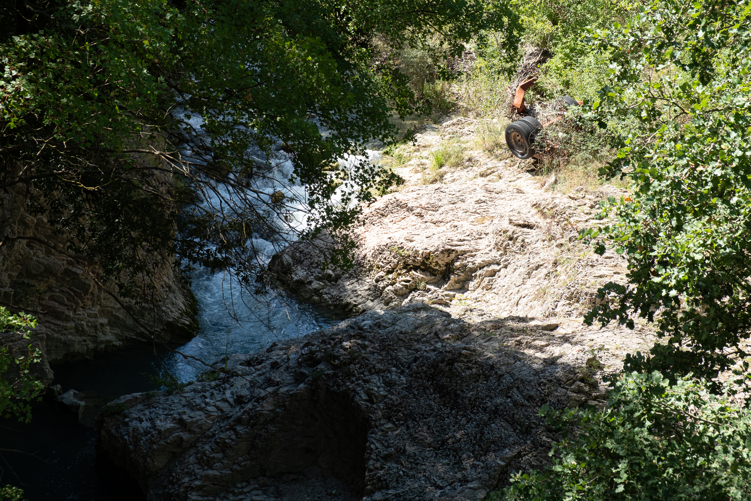 Wildbach zwischen Felsplatten – ein altes Fahrgestell im Gebüsch